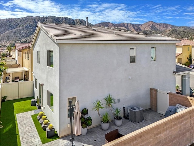 rear view of house featuring stucco siding, cooling unit, a mountain view, and fence