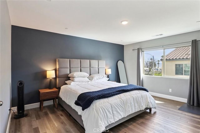 bedroom with an accent wall, baseboards, visible vents, and hardwood / wood-style floors