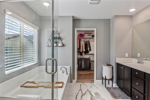 bathroom featuring a bath, marble finish floor, a walk in closet, and a wealth of natural light