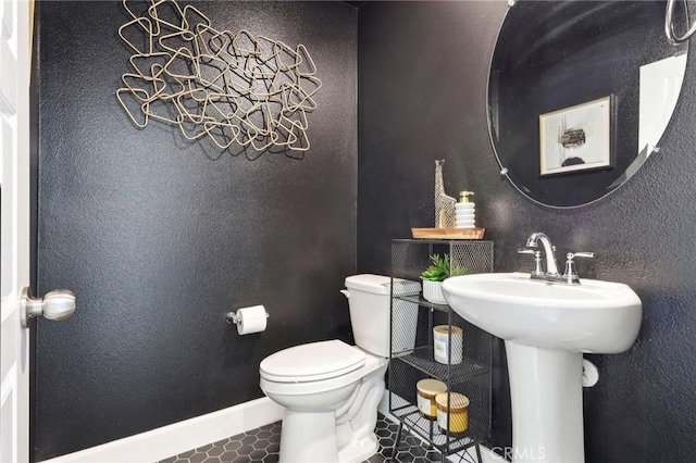 bathroom featuring tile patterned flooring, baseboards, a textured wall, and toilet