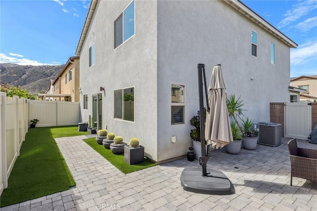 rear view of house with a lawn, a fenced backyard, central air condition unit, a patio area, and stucco siding