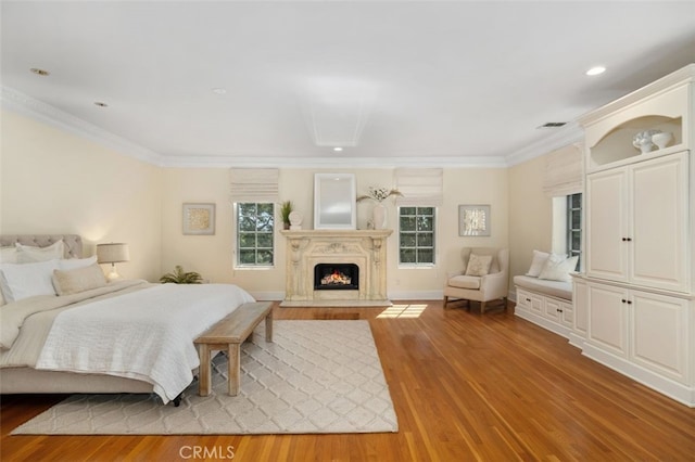 bedroom featuring light wood finished floors, a lit fireplace, visible vents, and crown molding