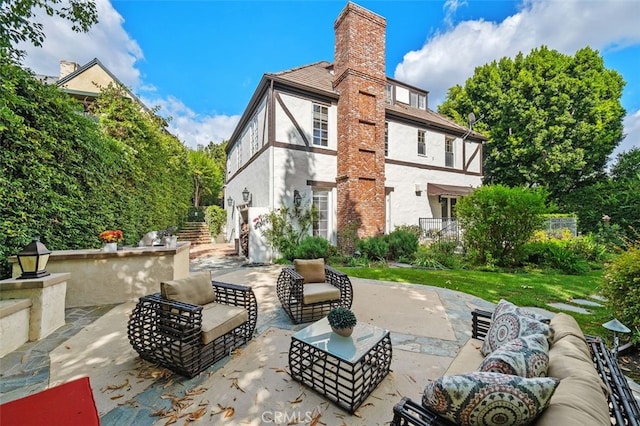 rear view of property featuring stucco siding, a chimney, an outdoor living space, and a patio