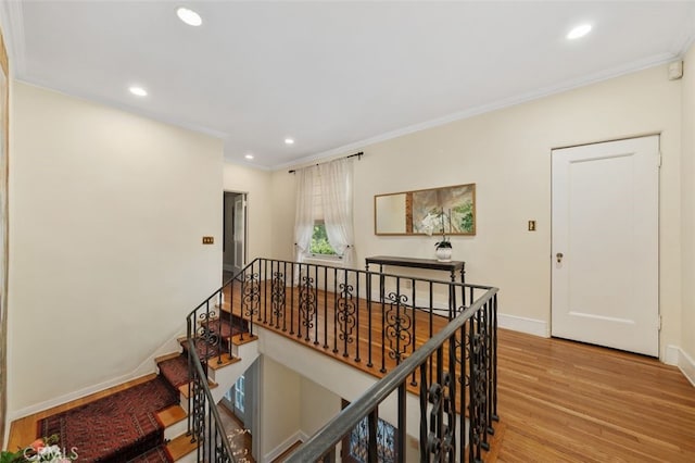 hallway featuring baseboards, ornamental molding, wood finished floors, an upstairs landing, and recessed lighting