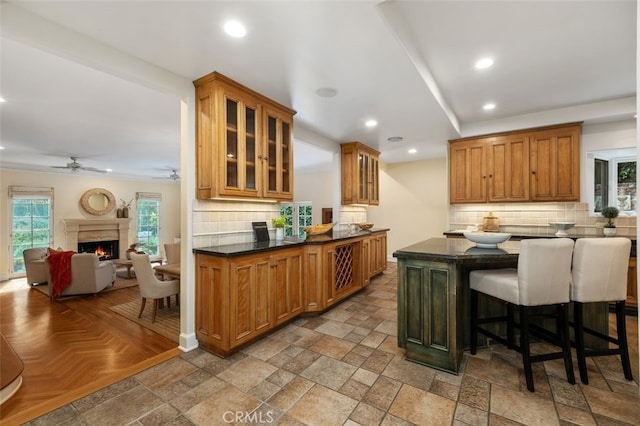 kitchen with a warm lit fireplace, stone tile floors, recessed lighting, tasteful backsplash, and glass insert cabinets