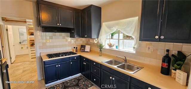 kitchen featuring black gas cooktop, tasteful backsplash, light countertops, a sink, and under cabinet range hood