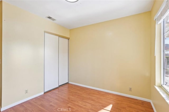 unfurnished bedroom with a closet, visible vents, light wood-style flooring, and baseboards