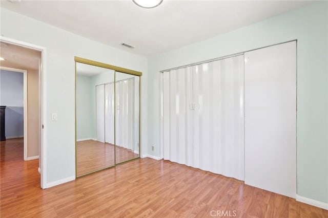 unfurnished bedroom featuring light wood-style flooring, baseboards, visible vents, and a closet