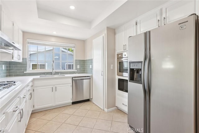 kitchen with backsplash, stainless steel appliances, white cabinets, light countertops, and a raised ceiling