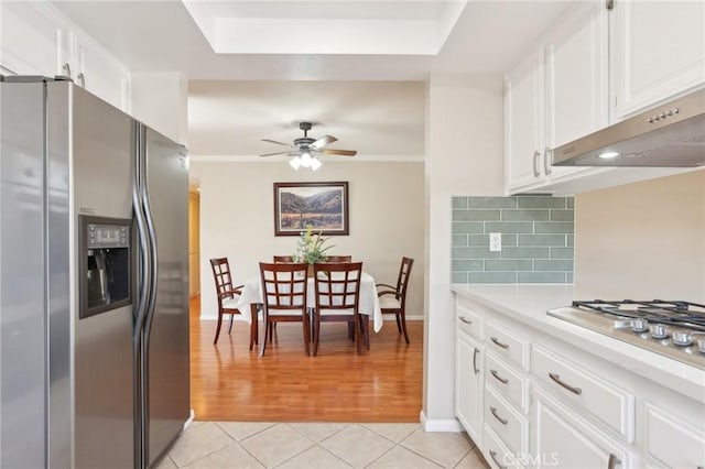 kitchen featuring under cabinet range hood, appliances with stainless steel finishes, light tile patterned flooring, light countertops, and decorative backsplash