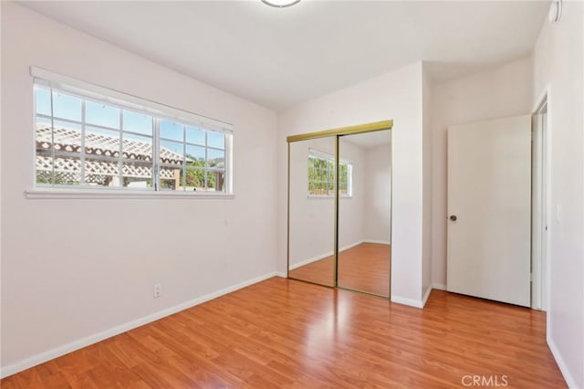 unfurnished bedroom featuring wood finished floors, baseboards, and a closet