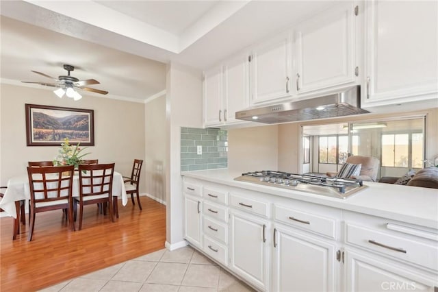 kitchen featuring light tile patterned flooring, light countertops, stainless steel gas stovetop, under cabinet range hood, and backsplash