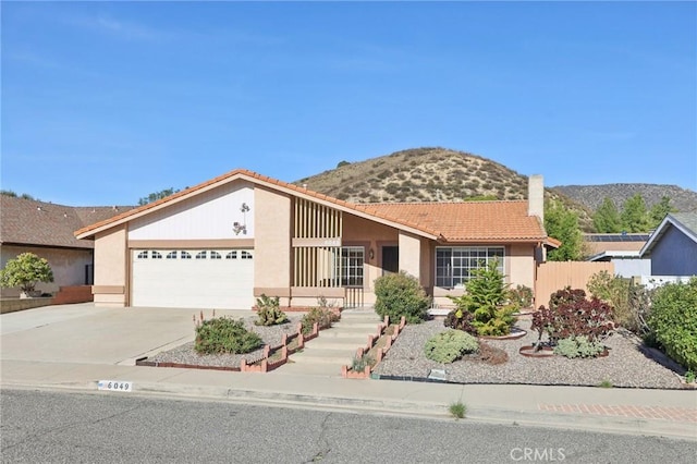 ranch-style house featuring driveway, a tile roof, a mountain view, an attached garage, and a chimney