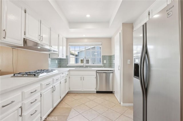 kitchen featuring a tray ceiling, white cabinets, under cabinet range hood, appliances with stainless steel finishes, and backsplash