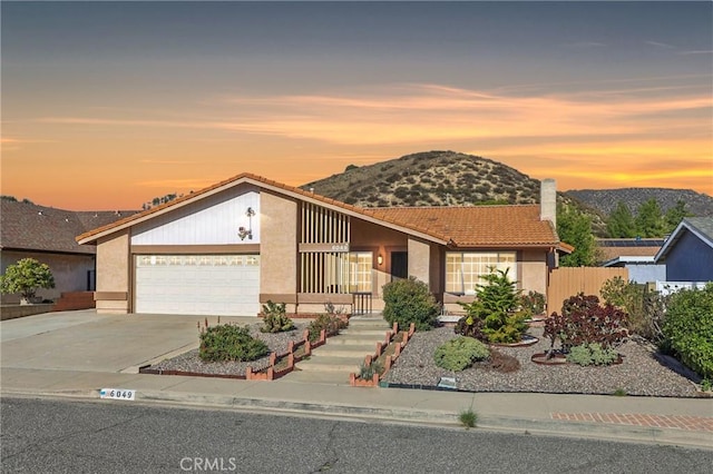 mid-century home featuring a mountain view, concrete driveway, an attached garage, and stucco siding
