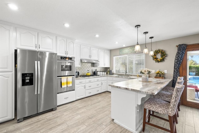 kitchen featuring a peninsula, a sink, appliances with stainless steel finishes, under cabinet range hood, and white cabinetry