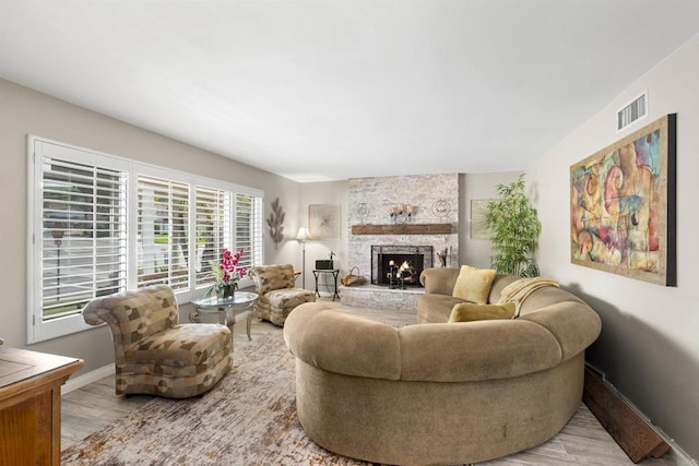 living room with light wood-type flooring, visible vents, baseboards, and a stone fireplace