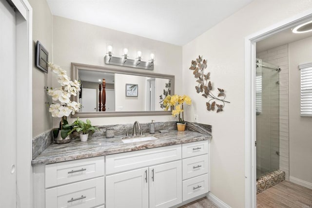 full bath with a shower stall, vanity, baseboards, and wood finished floors