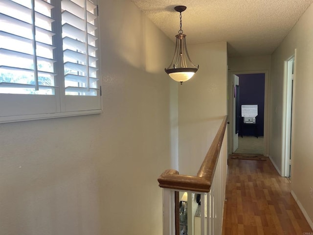 hallway featuring baseboards, an upstairs landing, a textured ceiling, and wood finished floors