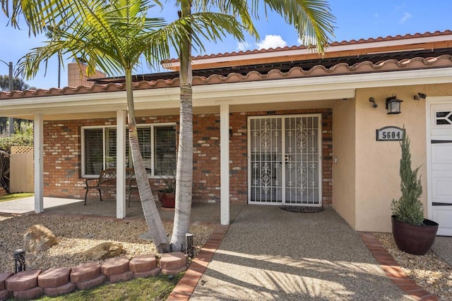 doorway to property with stucco siding, brick siding, and covered porch