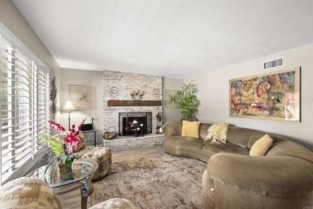 living room with visible vents, a stone fireplace, and wood finished floors