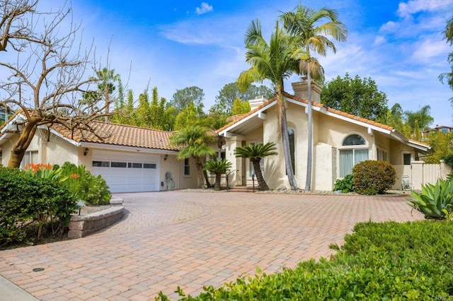 mediterranean / spanish-style house with a chimney, decorative driveway, an attached garage, and stucco siding