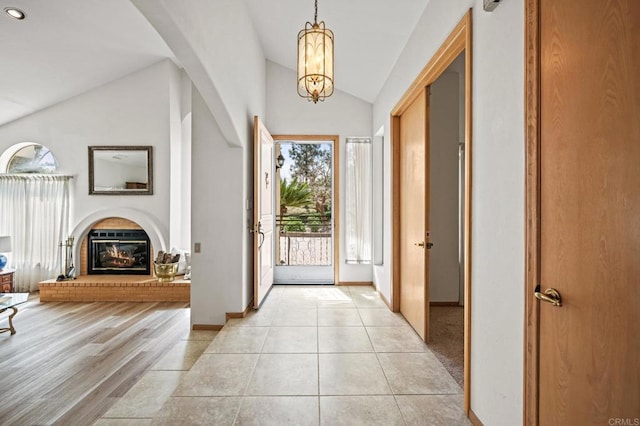 foyer entrance featuring lofted ceiling, light tile patterned flooring, a notable chandelier, baseboards, and a brick fireplace