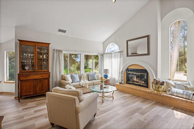 living area with visible vents, light wood-style floors, a glass covered fireplace, high vaulted ceiling, and baseboards