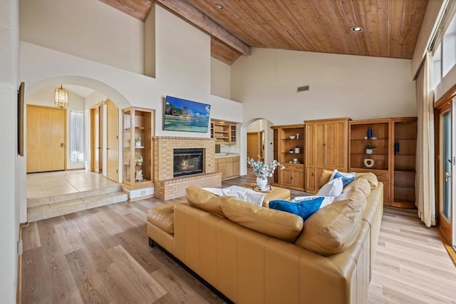 living room with light wood-type flooring, a brick fireplace, wood ceiling, and arched walkways