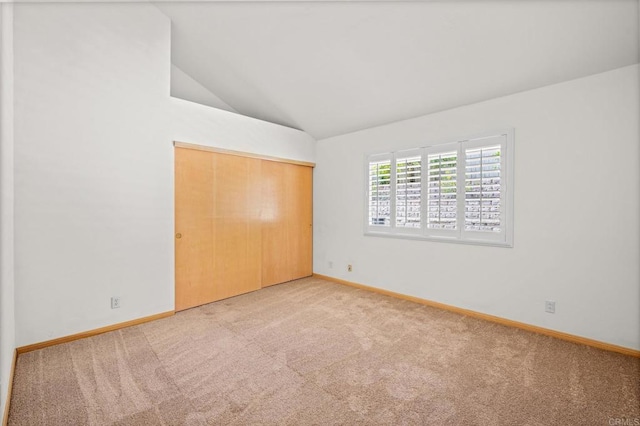 unfurnished bedroom featuring lofted ceiling, carpet, baseboards, and a closet