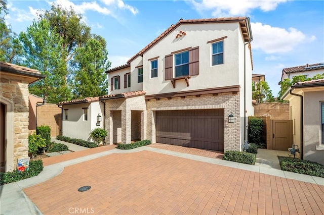 mediterranean / spanish-style home with decorative driveway, brick siding, stucco siding, a gate, and a tiled roof