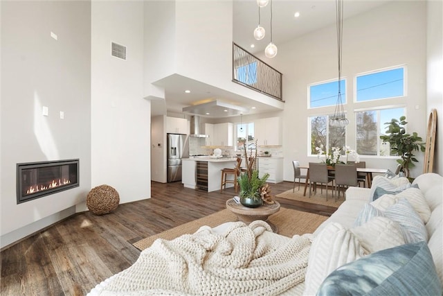 living room featuring a glass covered fireplace, dark wood-style flooring, visible vents, and recessed lighting