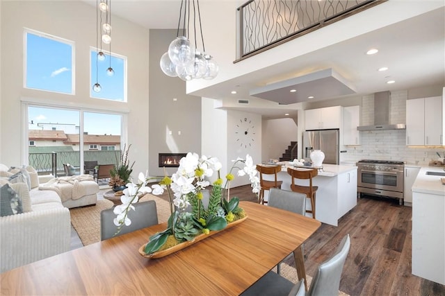 dining area with dark wood-style floors, a glass covered fireplace, recessed lighting, and stairs