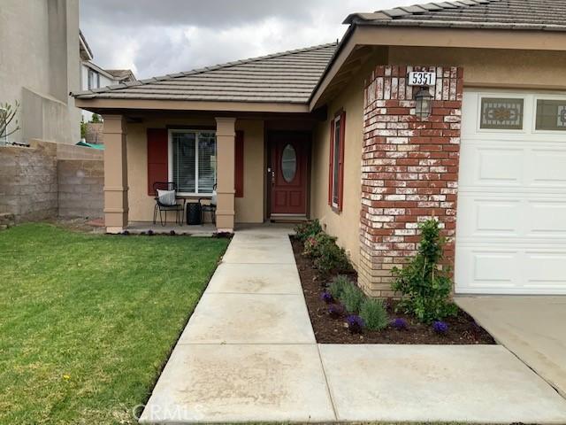 entrance to property with brick siding, a yard, a porch, an attached garage, and a tiled roof