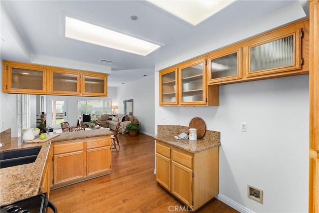 kitchen featuring a peninsula, light wood-type flooring, a sink, and light stone countertops