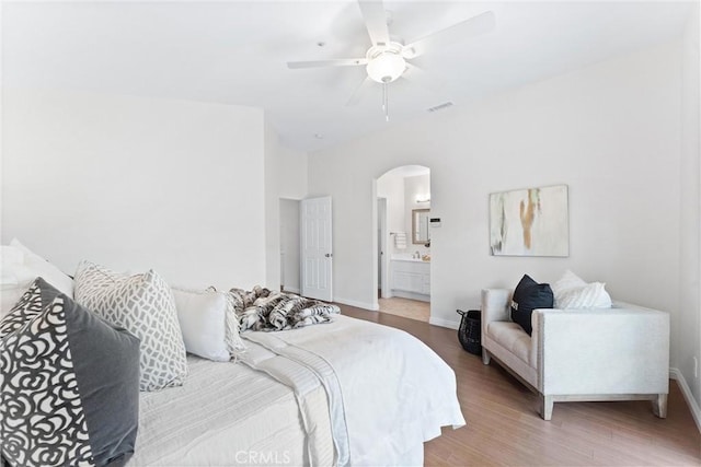 bedroom with arched walkways, wood finished floors, visible vents, and baseboards