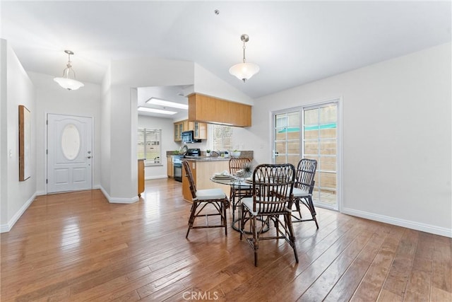 dining area with baseboards, vaulted ceiling, and light wood finished floors