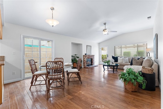 dining space with light wood finished floors, visible vents, a ceiling fan, a brick fireplace, and vaulted ceiling