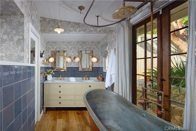 bathroom featuring wood finished floors, a freestanding tub, a sink, and wallpapered walls