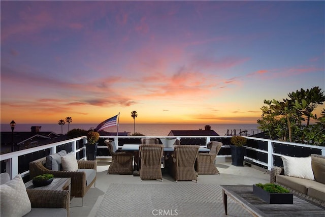 patio terrace at dusk featuring outdoor dining area, a water view, and an outdoor living space