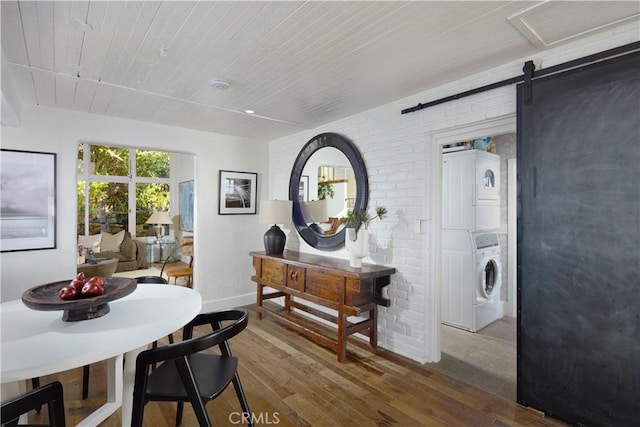 dining area featuring stacked washer and dryer, a barn door, wooden ceiling, brick wall, and wood finished floors