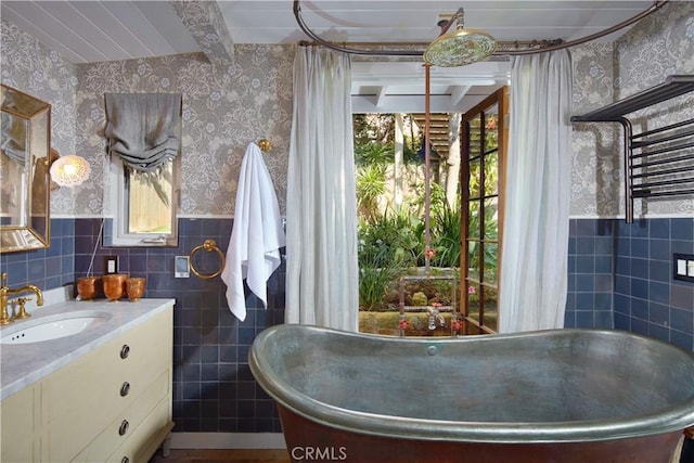 bathroom featuring a wainscoted wall, tile walls, a soaking tub, vanity, and wallpapered walls