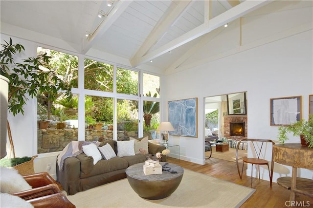 sunroom / solarium featuring vaulted ceiling with beams, a brick fireplace, and rail lighting