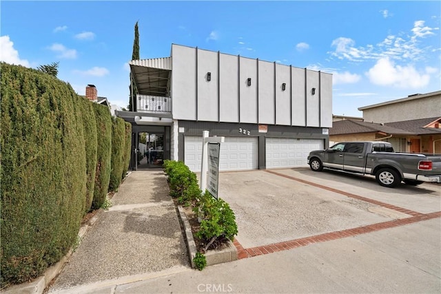 view of property with driveway, a balcony, and an attached garage