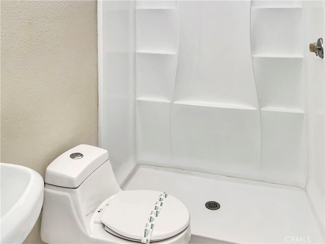 bathroom featuring a sink, a textured wall, a shower stall, and toilet