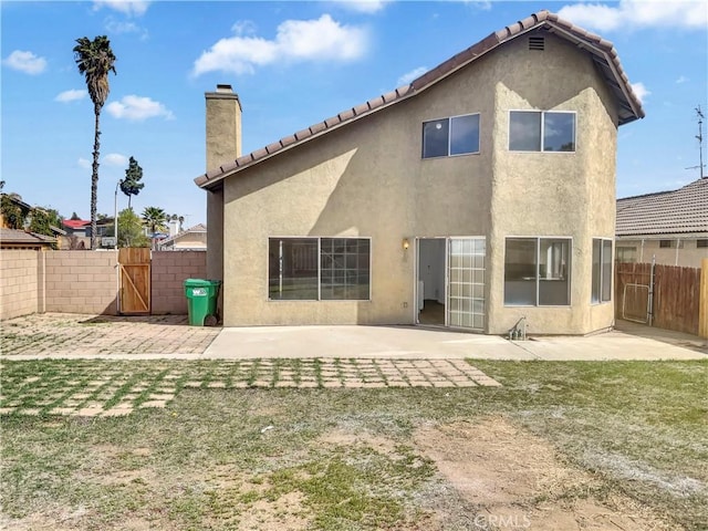 back of house featuring a chimney, a gate, fence, a patio area, and stucco siding