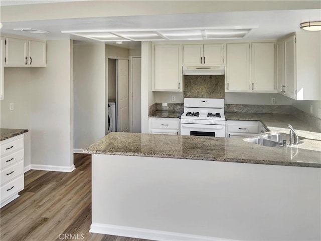 kitchen featuring white gas stove, under cabinet range hood, a sink, dark stone counters, and washer / dryer