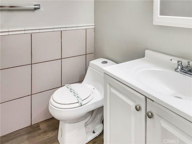 half bathroom featuring toilet, tile walls, wood finished floors, and vanity