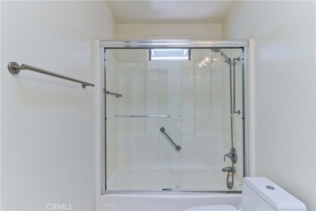 bathroom featuring toilet and bath / shower combo with glass door