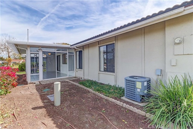 exterior space featuring a tile roof, a sunroom, central AC, and stucco siding